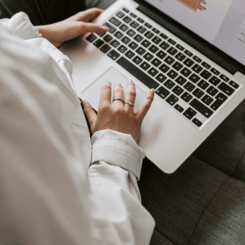 Person typing on a MacBook laptop while sitting on a couch.