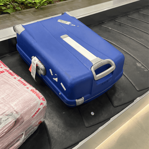 blue suitcase on an airport baggage carousel during a departure moment — letting go as a mother