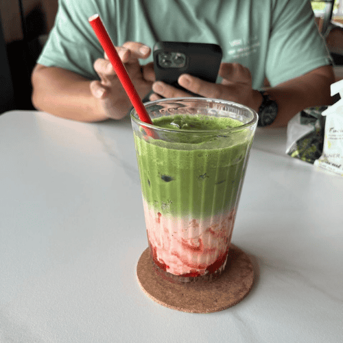 Letting go as a mother while sharing a quiet café moment with a matcha and strawberry layered drink on the table.
